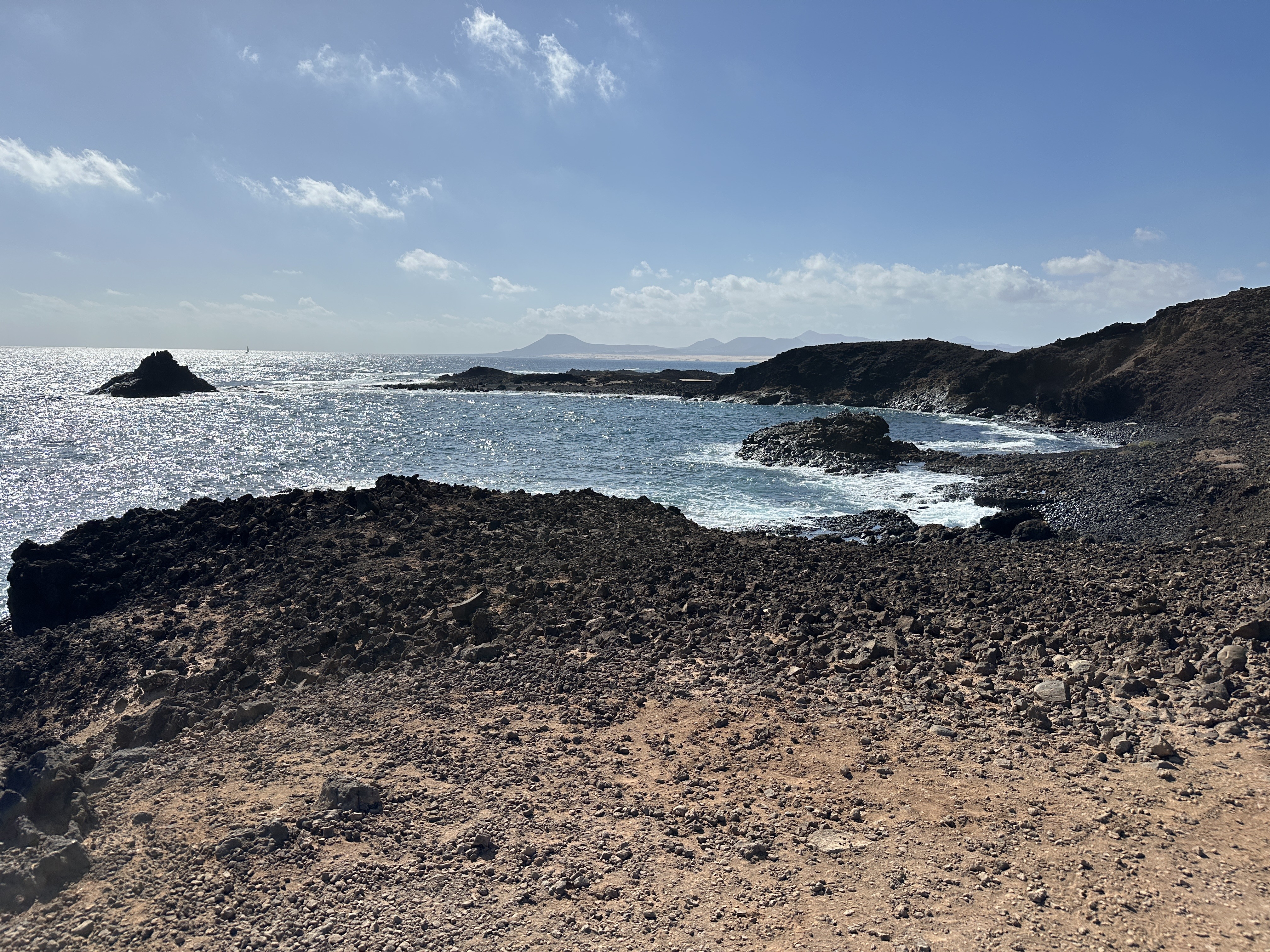 Rocky volcanic coastline of Isla de Lobos with crystal-clear water in a natural cove, Lanzarote visible across the strait