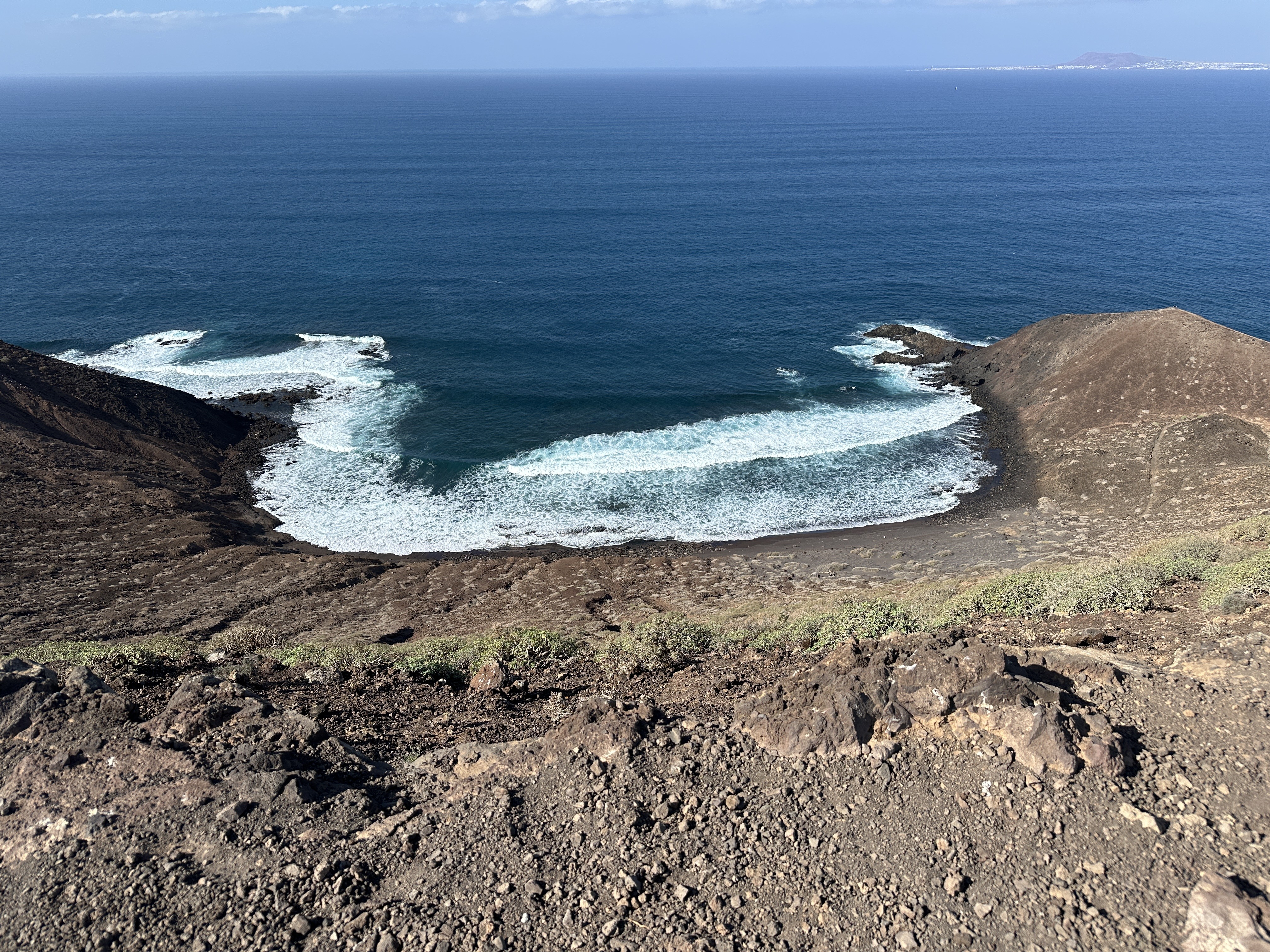 Aerial view of a cove on Isla de Lobos — waves breaking on black rock, turquoise water in the enclosed bay below