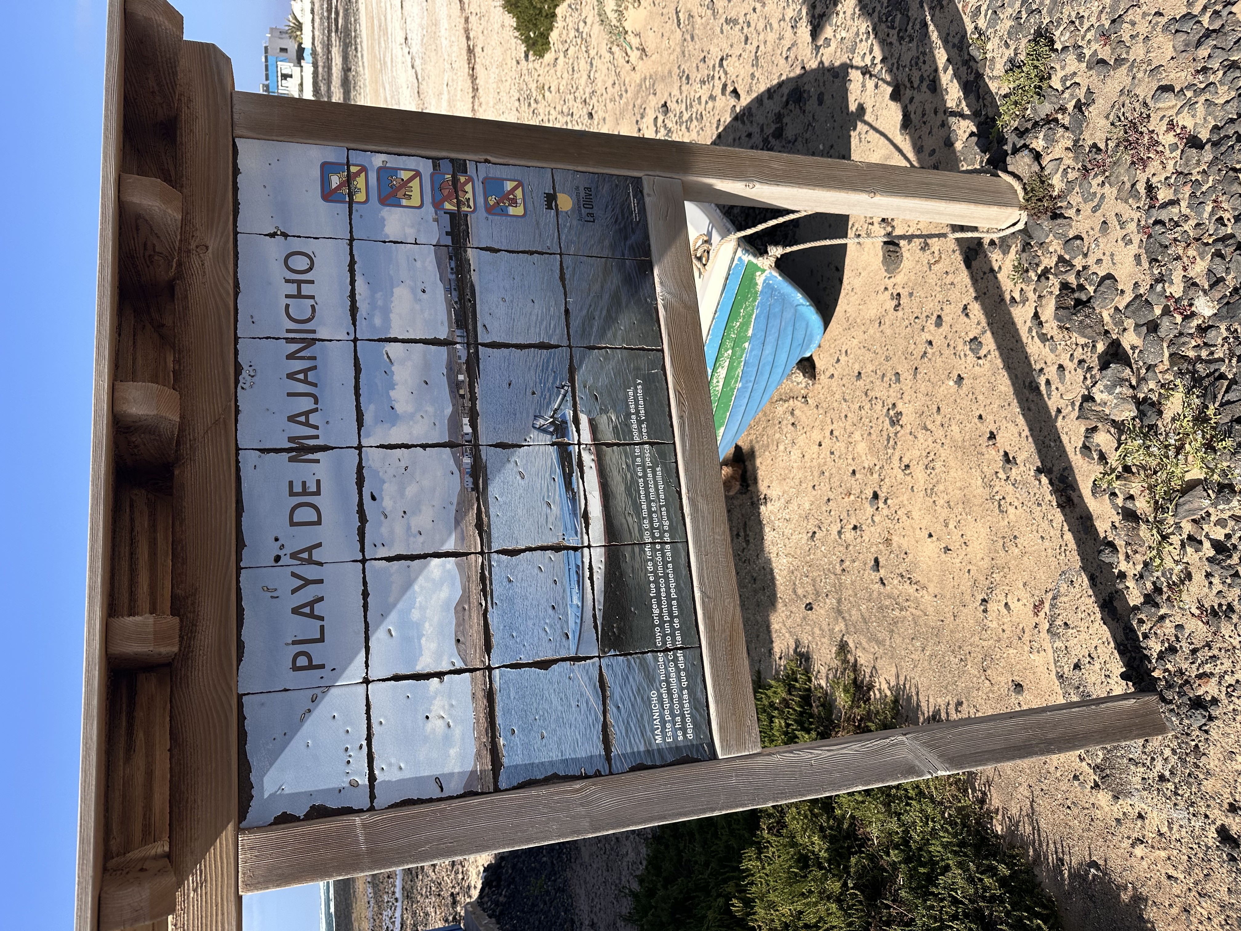 The official Playa de Majanicho information board at the beach entrance, with a colourful boat hull in the background