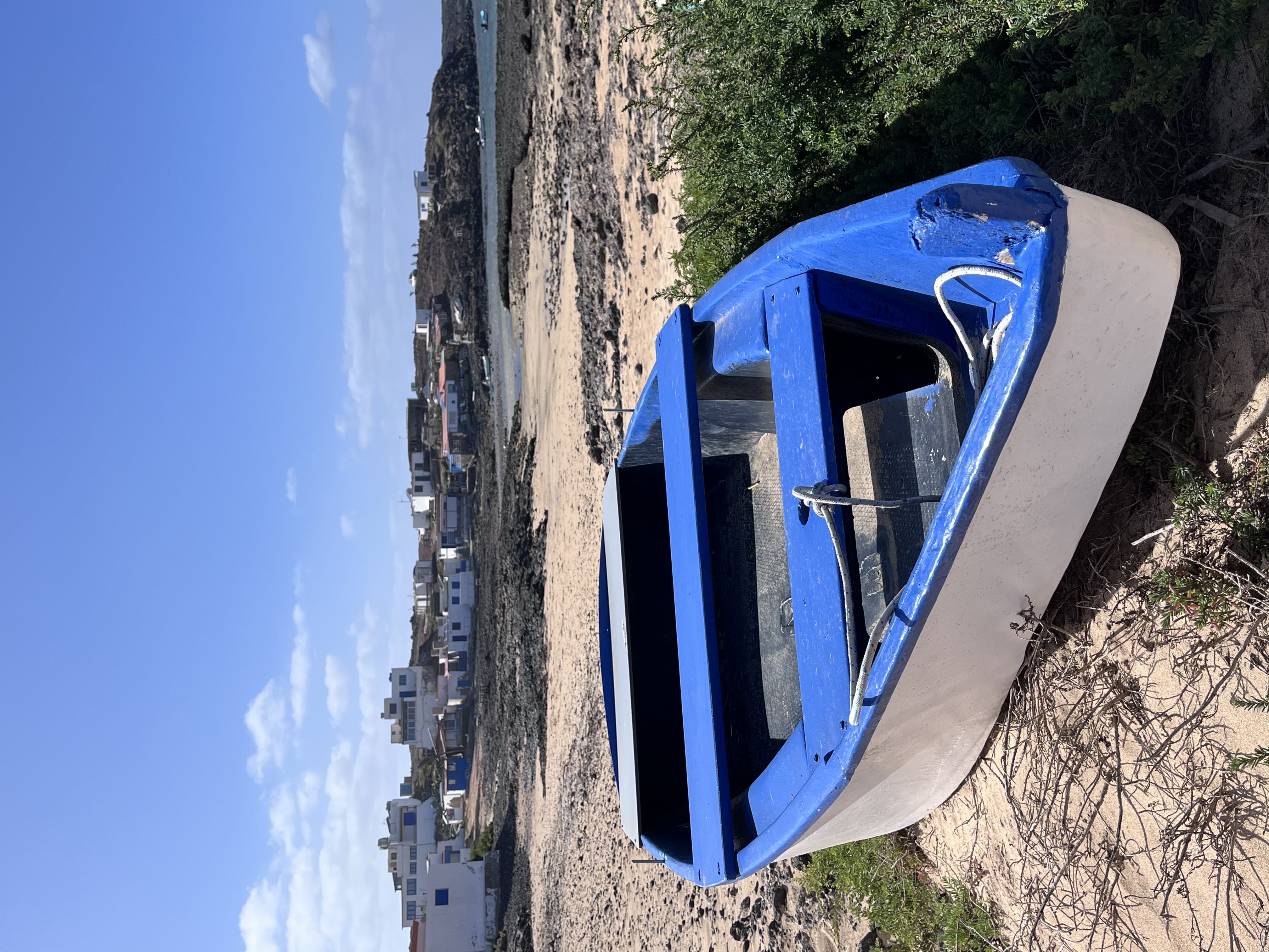 A blue-and-white fishing boat beached at Majanicho, with the whitewashed village rising behind it