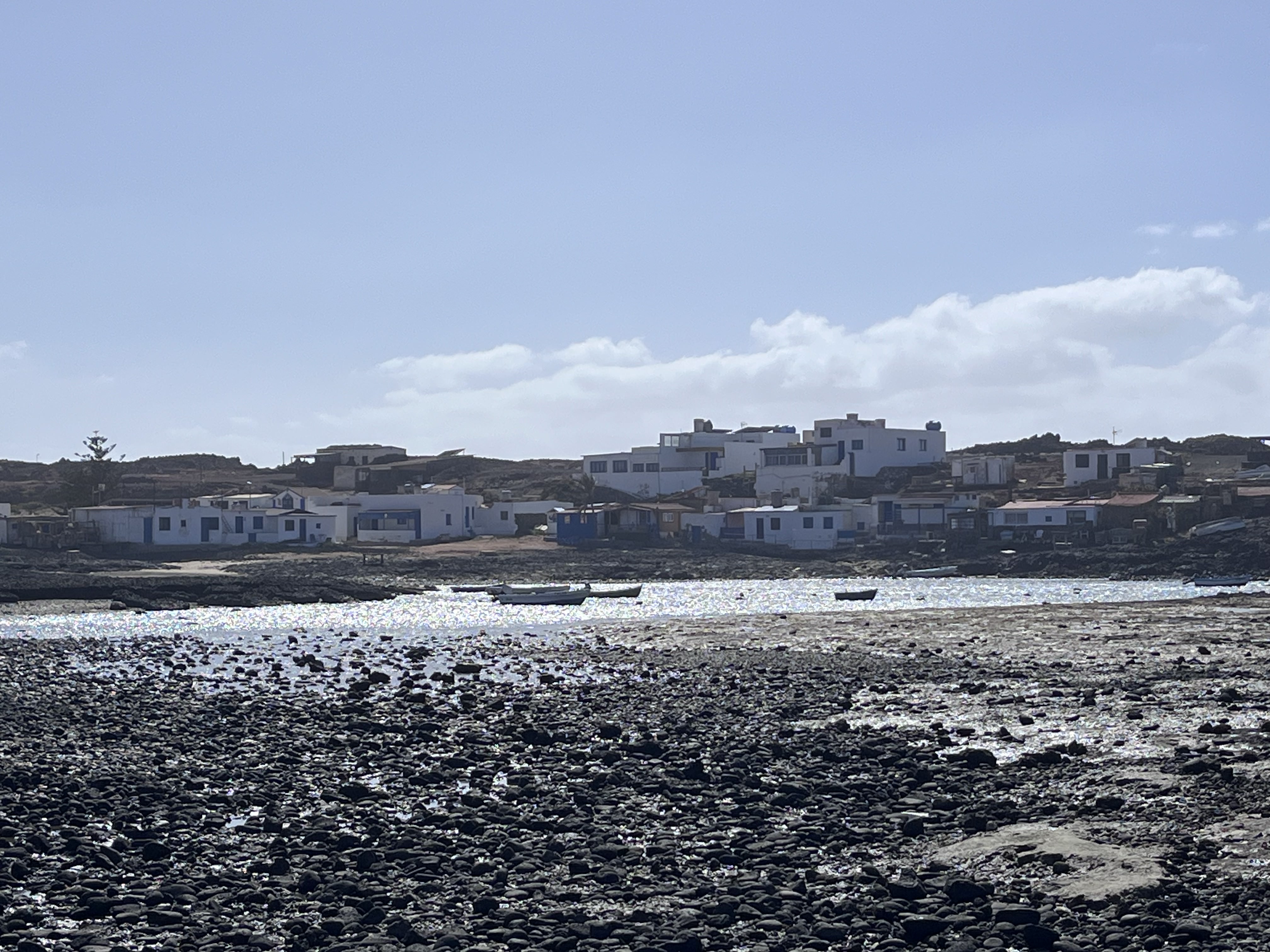 Majanicho village seen from across the bay — white houses on black volcanic rock, small boats moored in still water